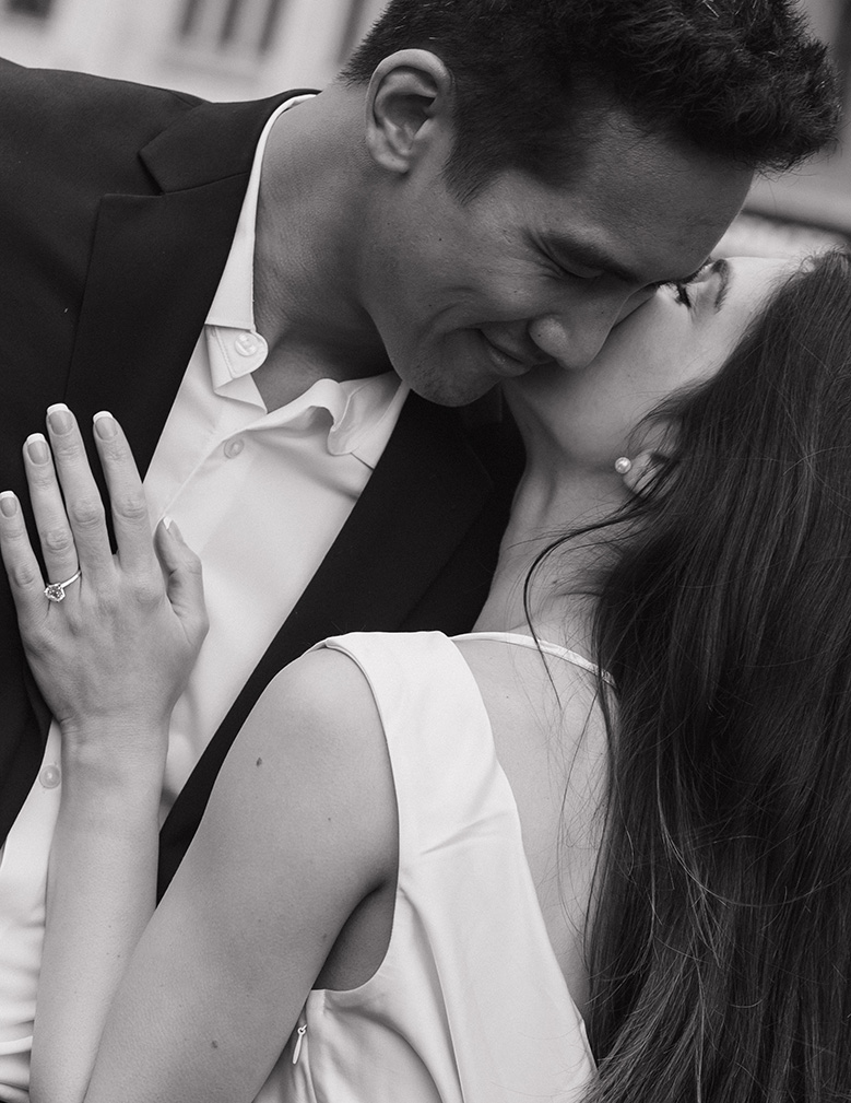 A couple shares an intimate moment, smiling tenderly at each other. She wears a ring, suggesting engagement. The tone is romantic and affectionate.