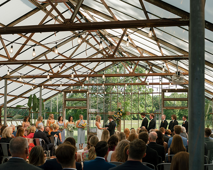 Wedding ceremony in Westerville, Ohio at Jorgensen Farms, with the couple exchanging vows. Guests are seated, and bridesmaids in light dresses stand nearby. Warm, joyful atmosphere.