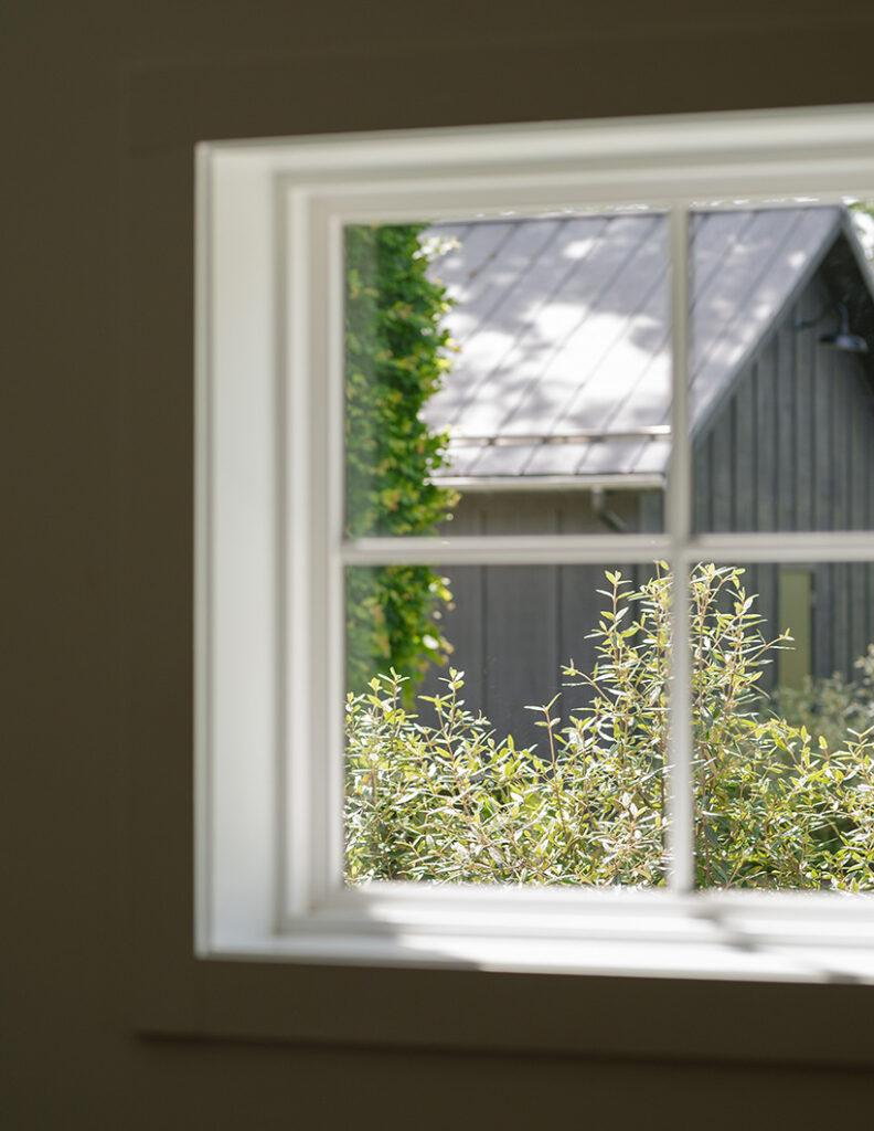 View through a window showing lush green bushes and Jorgensen Farms venue. Sunlight casts serene shadows, creating a peaceful atmosphere.