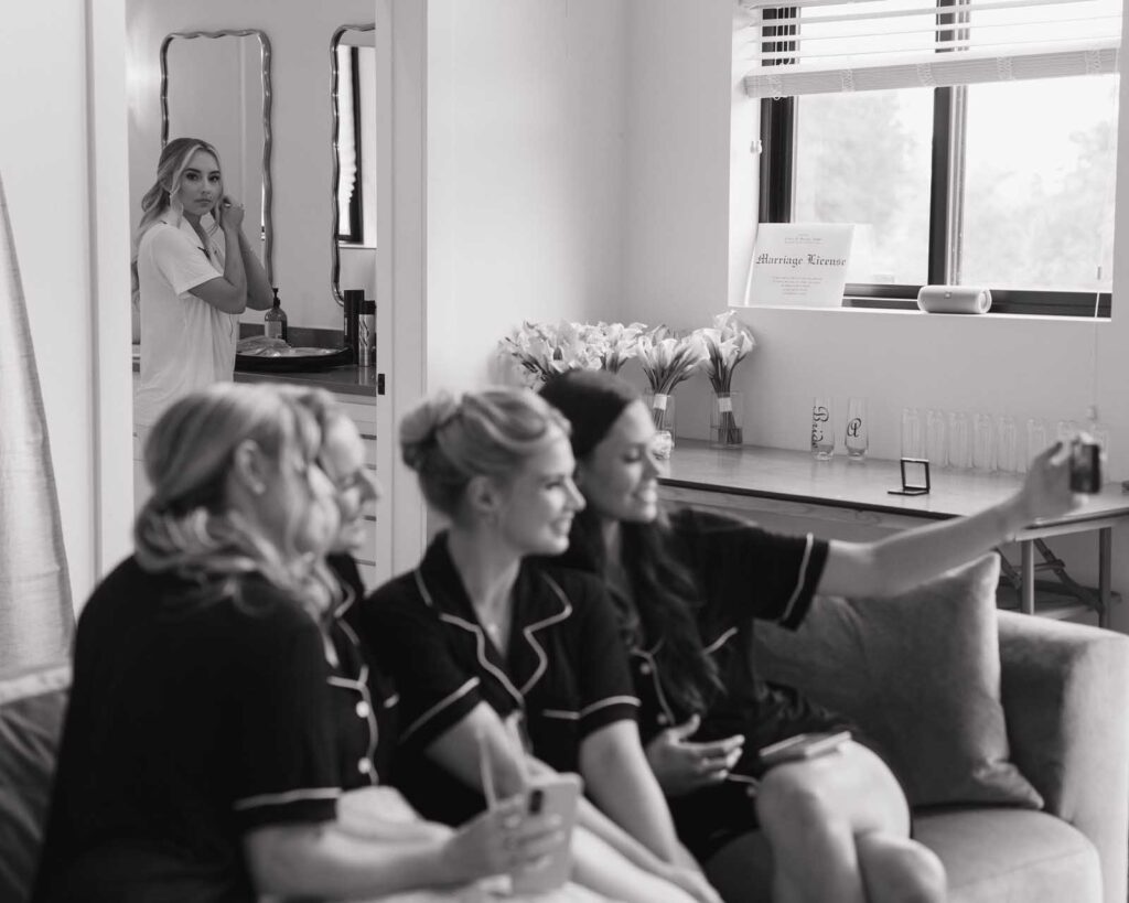 In a cozy room, four women in matching pajamas take a selfie on a couch.