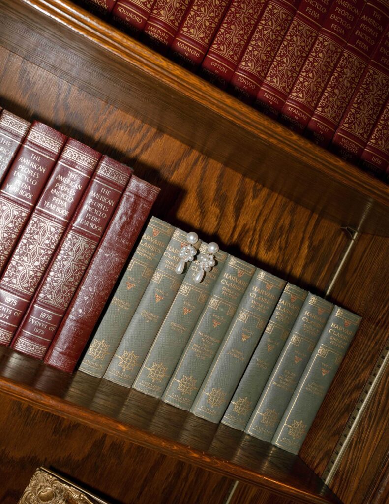 Bookshelf with red encyclopedias and green classics, showcasing elegant, decorative bindings. A pearl and jewel brooch adds a touch of sophistication.