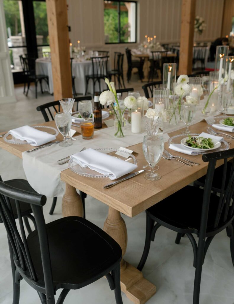 Elegant wooden table set for a formal dinner with crystal glasses, white plates, napkins, candles, and floral arrangements. Atmosphere is refined and inviting.