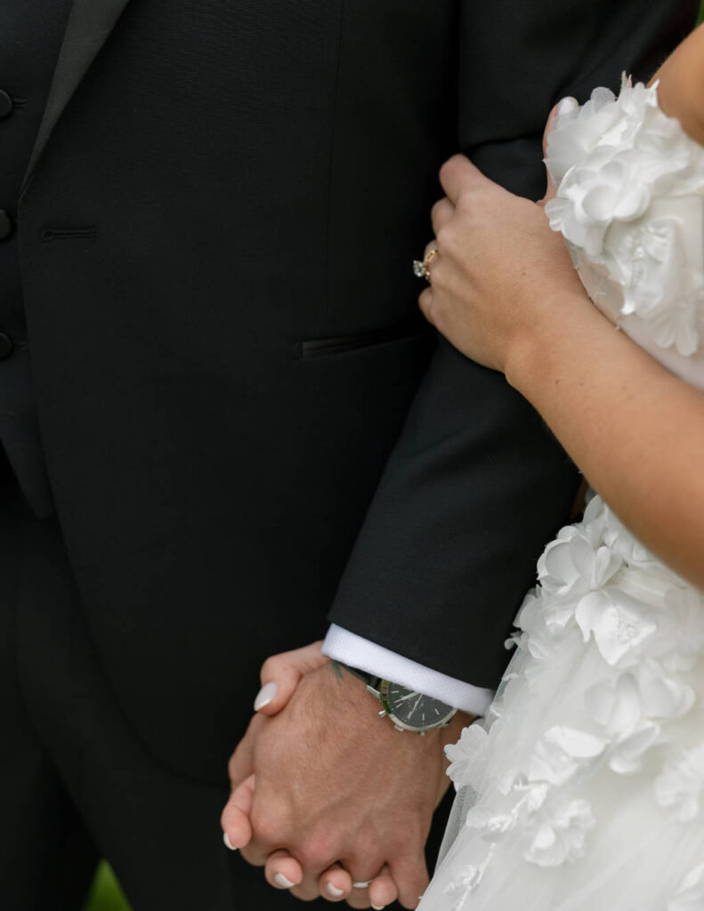 Close-up of bride and groom holding hands, highlighting wedding day details.