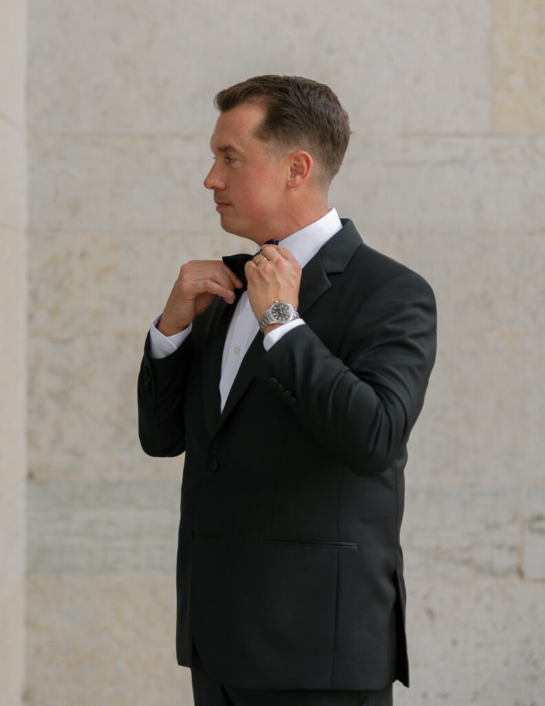 Groom adjusting his bowtie in front of an exposed brick wall at The Ellis.