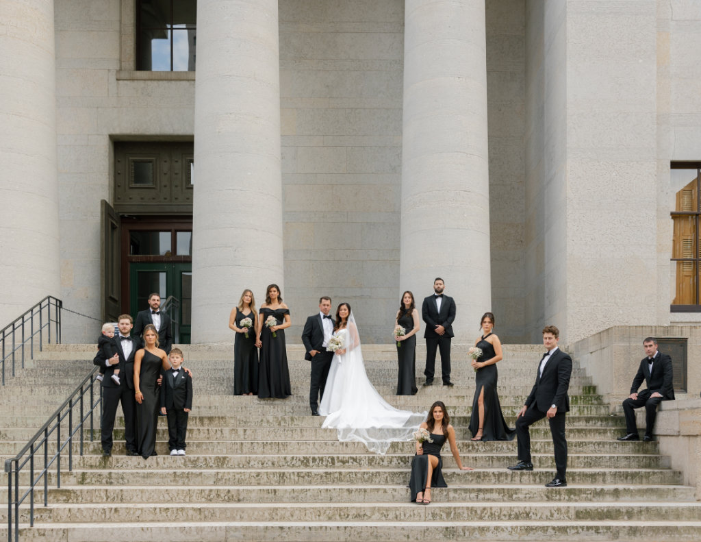 Bridal party posed with groom and bride with her veil flowing in front of the Ohio Statehouse.