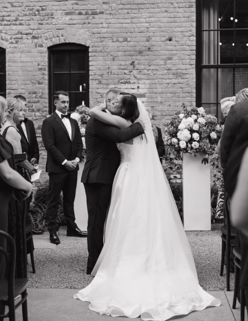 Newlywed portrait of The Walkers in front of the brick exterior at The Ellis.