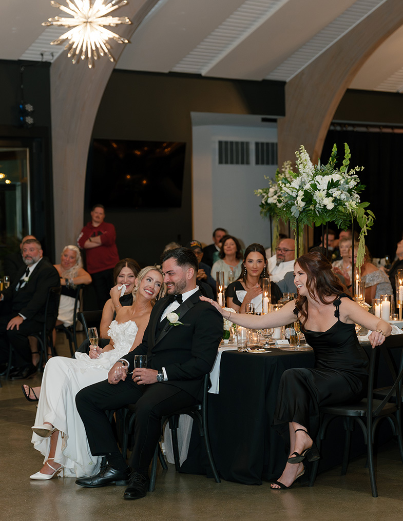 Couple smiling while giving a toast surrounded by friends and family.